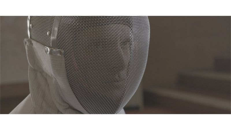 A close-up of a male fencer wearing an epee mask staring intently.