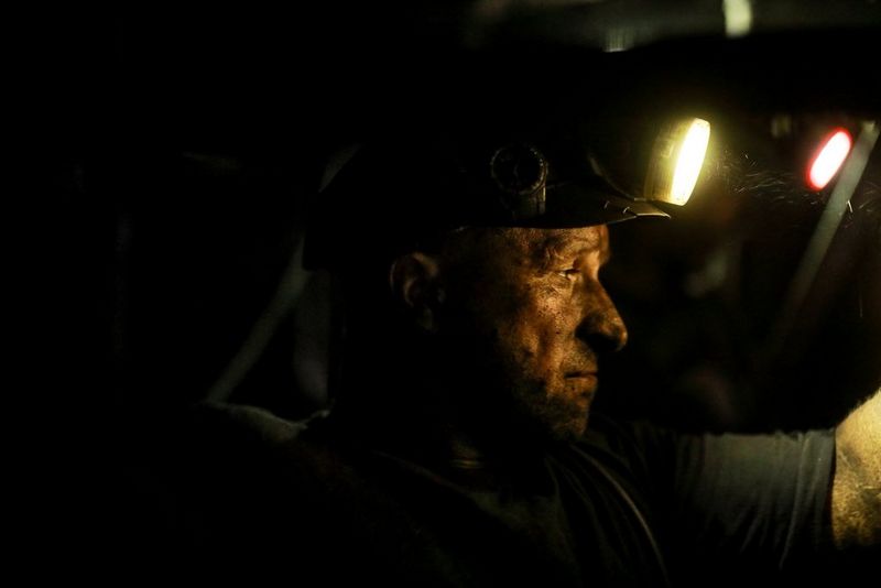 A photo taken in extreme low light on a Canon EOS R, showing a miner with coal dust on his face looking to the side, his face and arm lit only by his helmet lamp and a small light in the background.