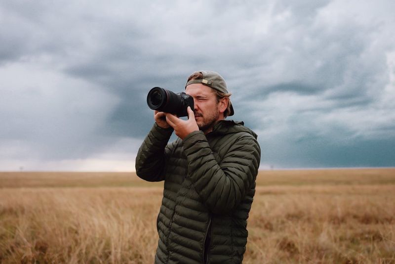Photographer Pie Aerts stands in a field, holding his Canon EOS R5 up to his face. 