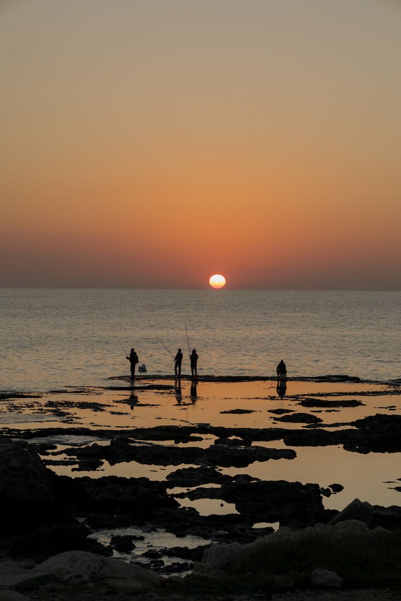 The sun sets on the horizon, giving the sky an orange hue over the sea in a photo by Aline Deschamps taken on a Canon EOS R8.