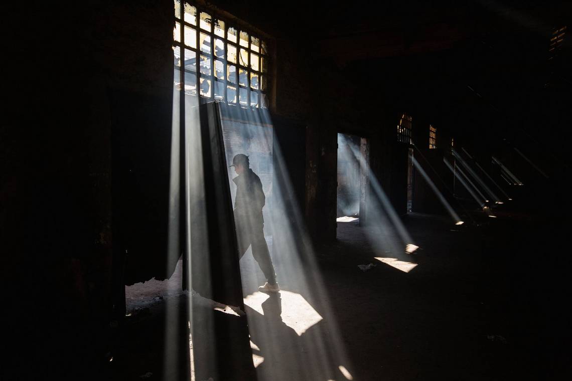 A man exits a dark warehouse as sunlight streams through the broken windows. Photo by Jędrzej Nowicki