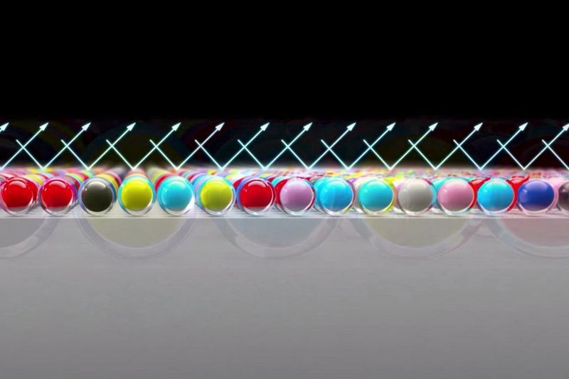 A diagram representing light reflecting evenly off the Chroma Optimiser layer on a photo print, with coloured ink droplets on the paper surface.