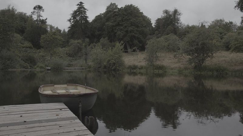A still from an ungraded video, shot with Canon Log, showing a boat tied to a jetty with greenery in the background, appears washed-out and low-contrast.