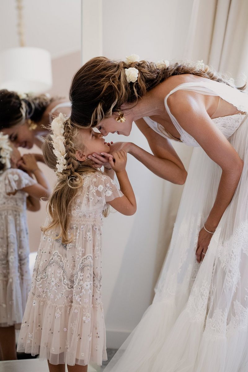Dressed in their wedding attire, a bride leans down to her young bridesmaid to rub noses playfully.