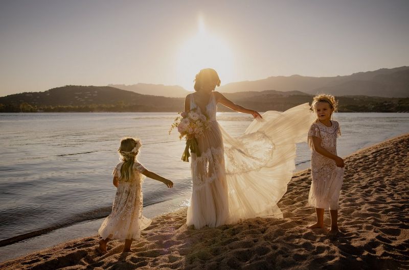 A bride and her two young bridesmaids twirl their dresses at sunset on a deserted beach.
