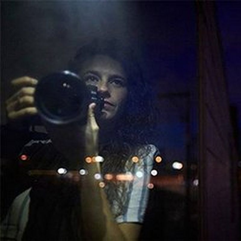 A headshot of Bieke Depoorter holding a camera in low light.