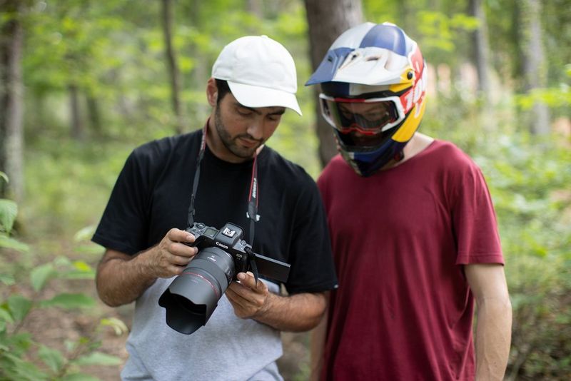 Two men discuss an image taken on a Canon EOS R5 camera while standing in a forest. 