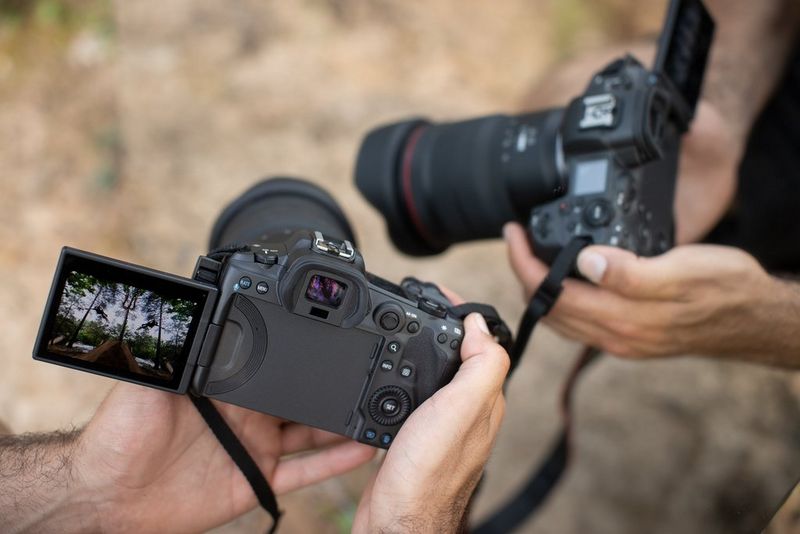 A mirror image of a man holding a Canon EOS R5 camera with the touchscreen in focus showing another mirror image. 