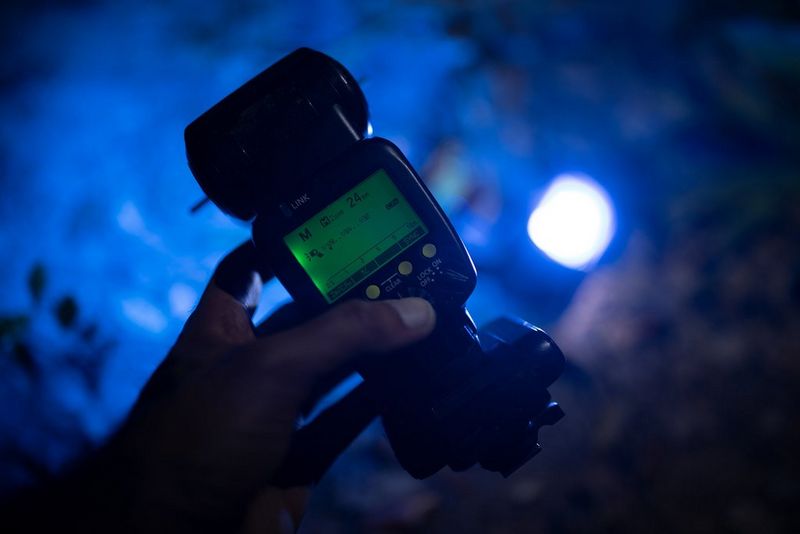 A hand holds a Canon Speedlite 600EX II-RT. The dark background is bathed in blue light.