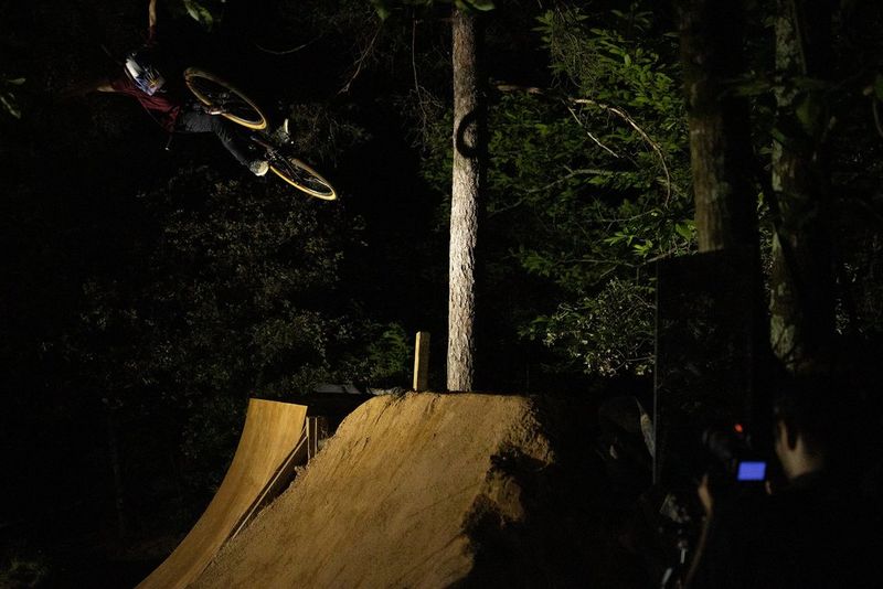 A photographer takes a night-time shot of a stunt rider launching off a ramp with his arms outstretched.