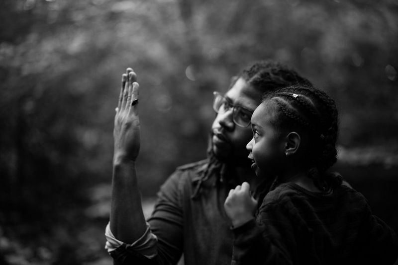 A black and white image of a man holding up his hand to show a young girl a beetle on his little finger.