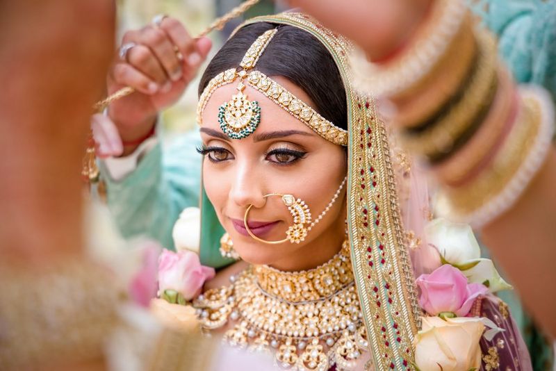 A head and shoulders portrait of a bride wearing elaborate gold jewellery including a nose ring and head piece.
