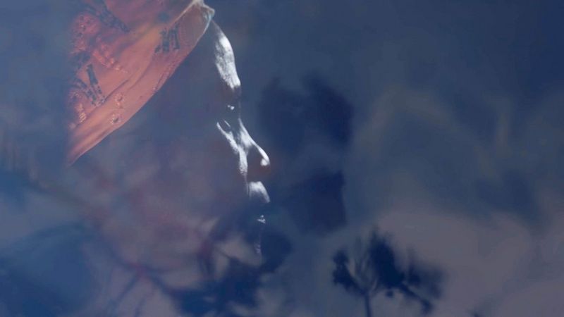 A still from a video showing a woman in side profile, her face partially obscured by shadows, shot by Laura El-Tantawy for her series Carrying Life: Motherhood and Water in Malawi.