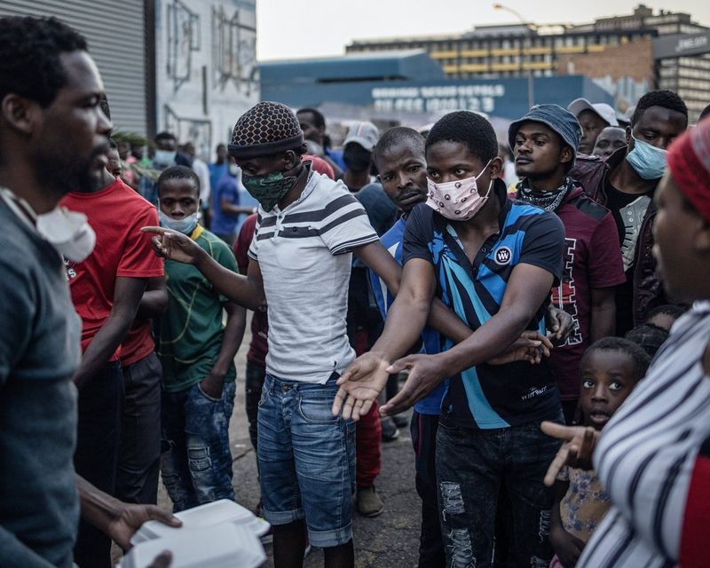 A man stands holding food boxes as a crowd of people queue, one man stretching out his hands towards the boxes as he is held back by the man next to him.