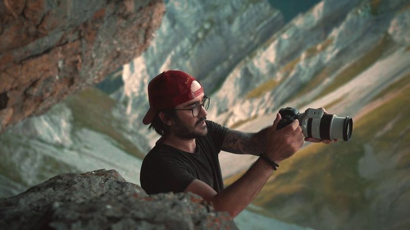  Photographer Steven Herteleer stands amongst rocks in the mountains, holding a Canon camera in front of him and looking at the viewscreen, in a still from the Canon Learning Series.