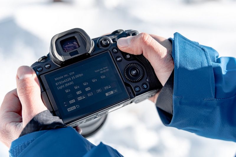 A close-up of a person's hands holding a Canon EOS R5, with the screen displaying settings.