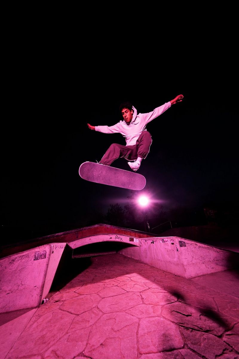 A man performing a skateboard trick at night, illuminated by purple lighting.
