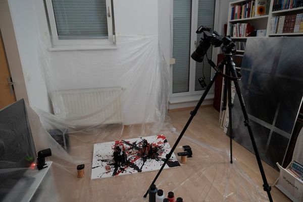 A Canon EOS R on a tripod is directed at a paint-splatter canvas on the floor. The room is covered in plastic sheeting.
