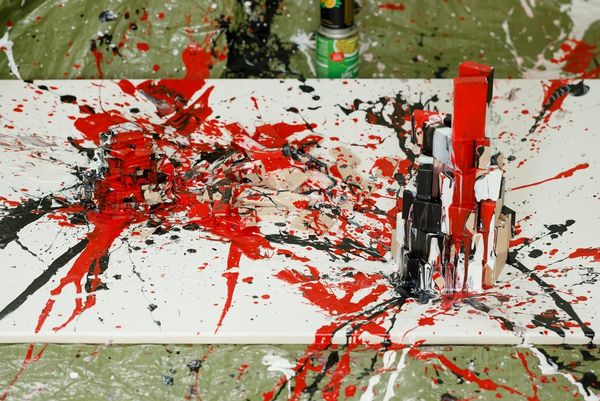 A canvas on the floor covered in splatters of red, black and white paint. 