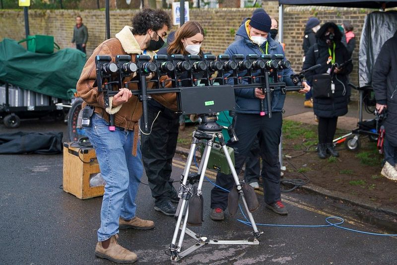 Three masked crewmembers, all wearing warm coats and jeans, adjust an elevated bar cam of Canon EOS R5 cameras on an outdoor set.