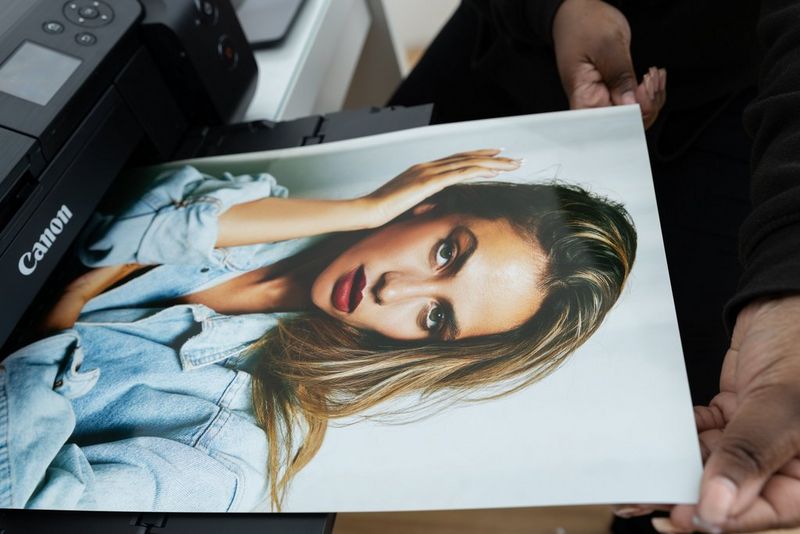 A print of a model with long blonde hair wearing a denim jacket emerges from a Canon PIXMA printer.