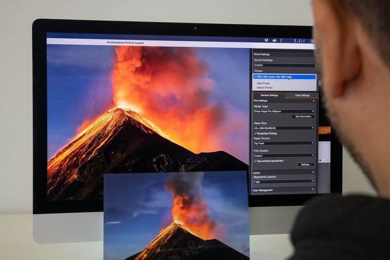A man adjusts the print settings using Canon Professional Print & Layout software on his computer. On his screen is a picture of Guatemala's Fuego stratovolcano.