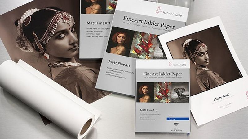 A photo paper roll, paper packaging and images printed on Hahnemühle paper all spread on the table.