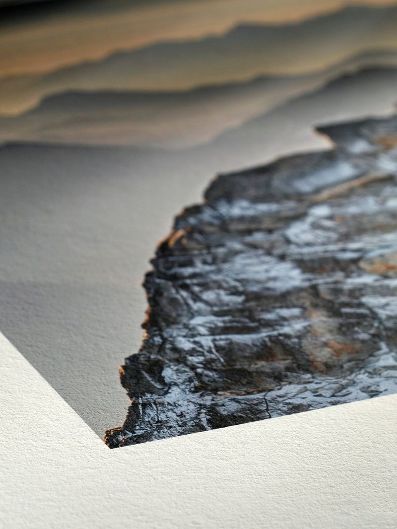 A close-up of the corner of a photo print on lightly textured hemp paper, showing a large rock in front of a misty, mountainous landscape.