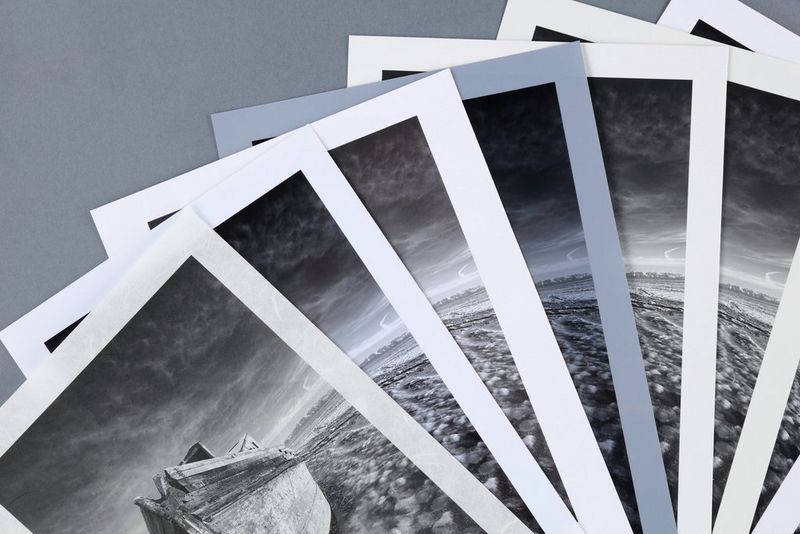 Seven prints, fanned out, of a monochrome photograph of a boat printed on different types of photo paper.