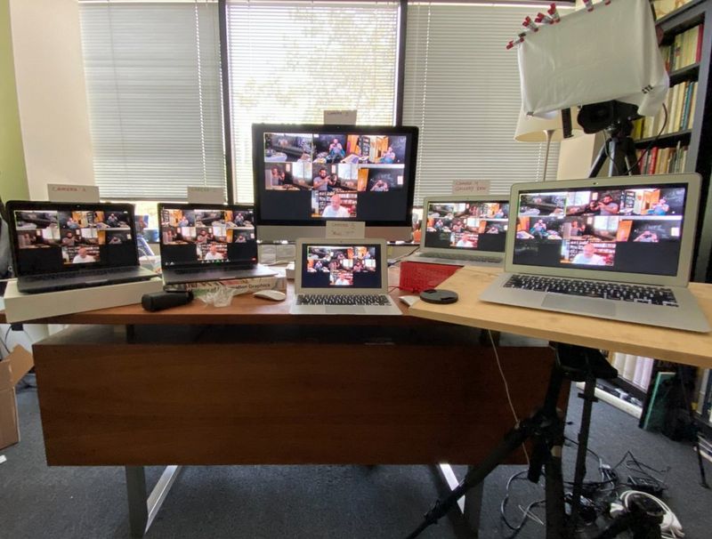 A collection of laptops on a desk all showing the same image of a group of people chatting remotely.