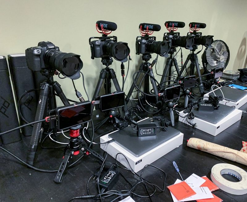 An array of Canon EOS R cameras, tripods, lights and computers on a desk.