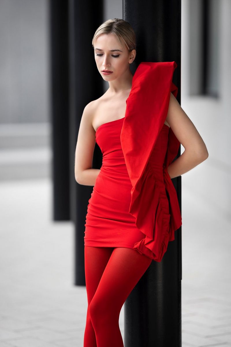 A woman wearing a red top and red bottoms leans against a black pillar and looks down at the ground. Taken by Sascha Hüttenhain with a Canon RF 135mm F1.8L IS USM lens.