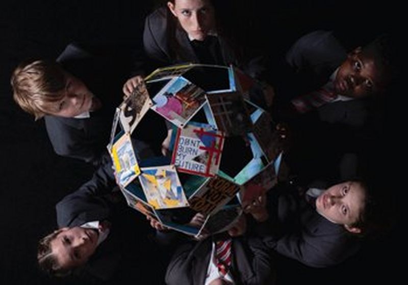 Taken from above, six children, on the left, right top and bottom of the photo, hold a globe made of photographs and raise their solemn faces to the camera. The clearest photo, closest to the camera displays the words ‘don’t burn my future’.