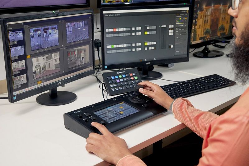 A man working on a Canon RC-IP100 PTZ controller connected to two digital screens.