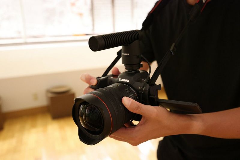 Hands holding a Canon camera with a Canon RF 10-20mm F4L IS STM lens attached.