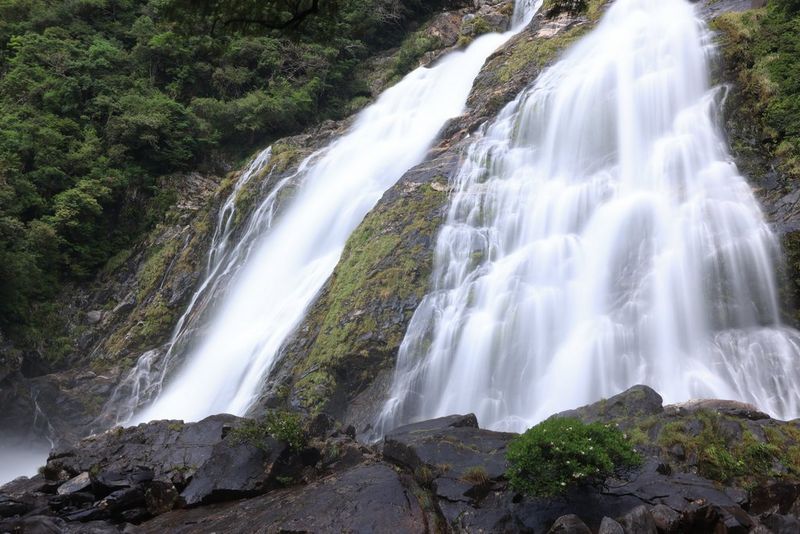 Water cascading down big mossy rocks. The water is blurred because of the camera's slow shutter speed.