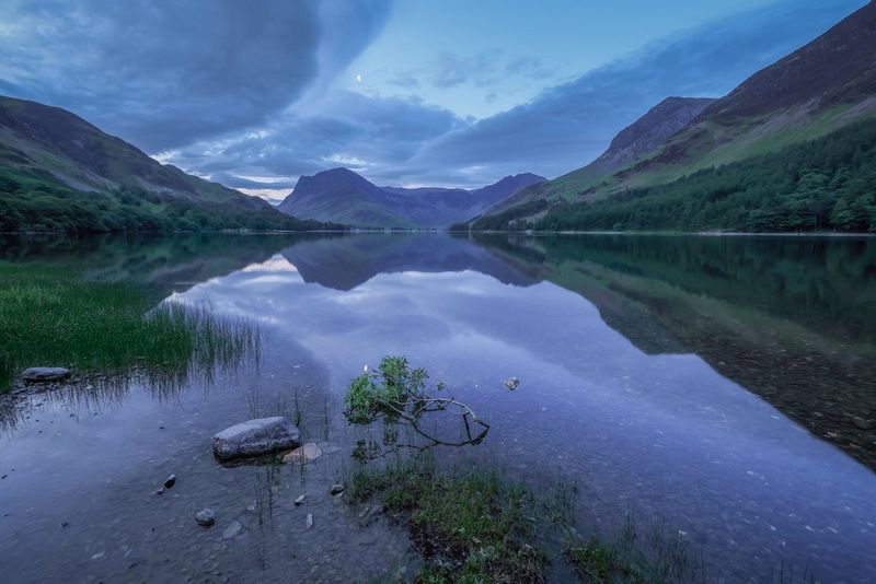 Cloud formations reflected on the surface of a still lake surrounded by mountains.