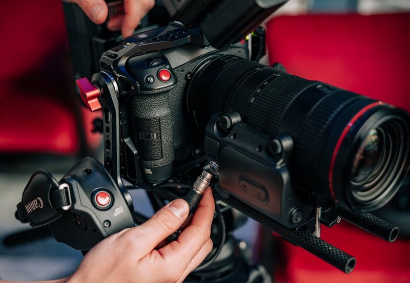 A user about to attach the cable from a Power Zoom Adapter PZ-E2B to the 20-pin socket on a Canon RF 24-105mm F2.8L IS USM Z lens.