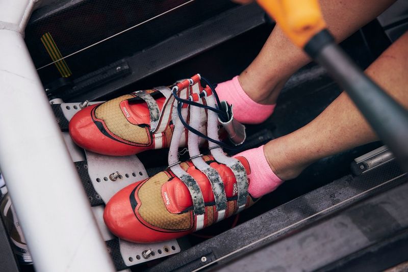 A close-up of a rower's feet, clad in red shoes and pink socks, in the bottom of a boat.