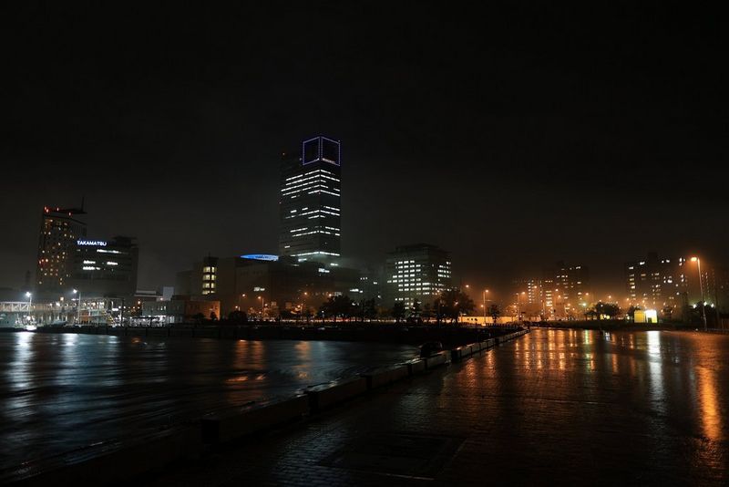 A cityscape lit up at night with the buildings' reflections visible in the water in the foreground. Taken on a Canon EOS R6 with a Canon RF 24mm F1.8 MACRO IS STM lens.