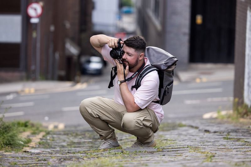 Photographer Andres McNeill crouches down to take a shot with a Canon RF 28mm F2.8 STM lens on a moss-covered cobbled street. 
