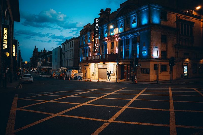 A person walking in front of a theatre at night is illuminated by the lights emanating from the building. Taken by Andres McNeill with a Canon RF 28mm F2.8 STM lens.