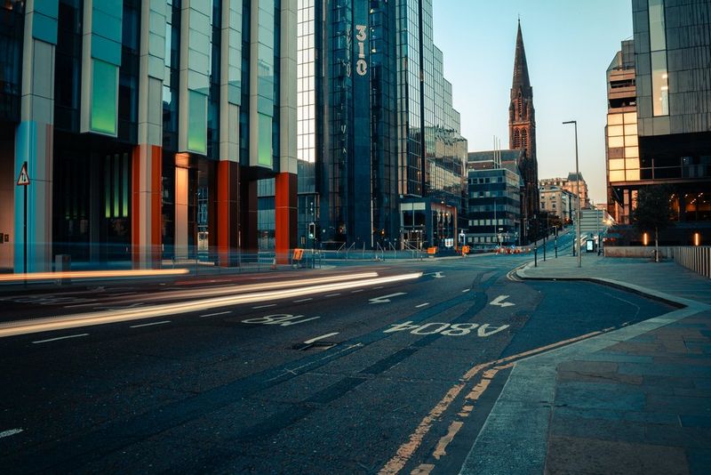 Car light trails in early evening light on a city street populated by tall buildings, taken by Andres McNeill with a Canon RF 28mm F2.8 STM lens.