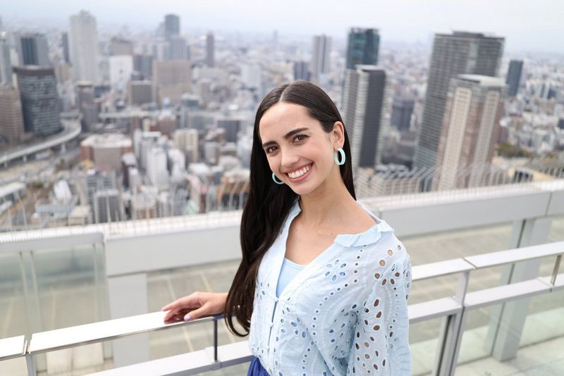 A smiling tourist stands on a balcony with a cityscape stretching out behind them, taken on a Canon EOS R8 with a Canon RF 28mm F2.8 STM lens.
