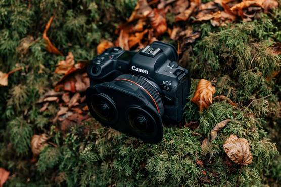 A Canon EOS R5 camera with a Canon RF 5.2mm F2.8L Dual Fisheye lens positioned on a mossy surface next to fallen autumn leaves.
