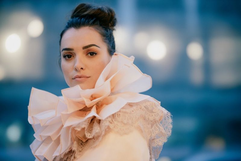 An image shot in low light of a model in a ruffled collar posing in front of blurred streetlights. Taken on a Canon EOS R with a Canon RF 85mm F1.2L USM DS lens. 