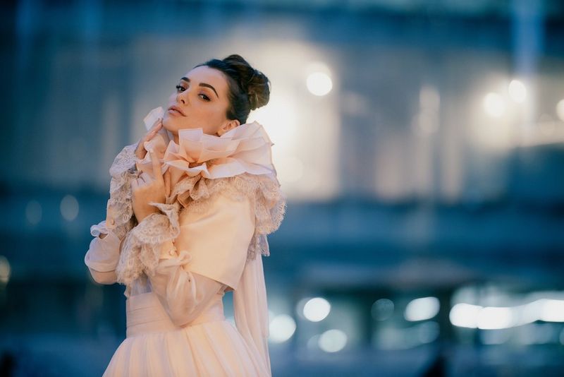 An evening portrait of a young woman in a ruffled off-white wedding dress, with the background out of focus.