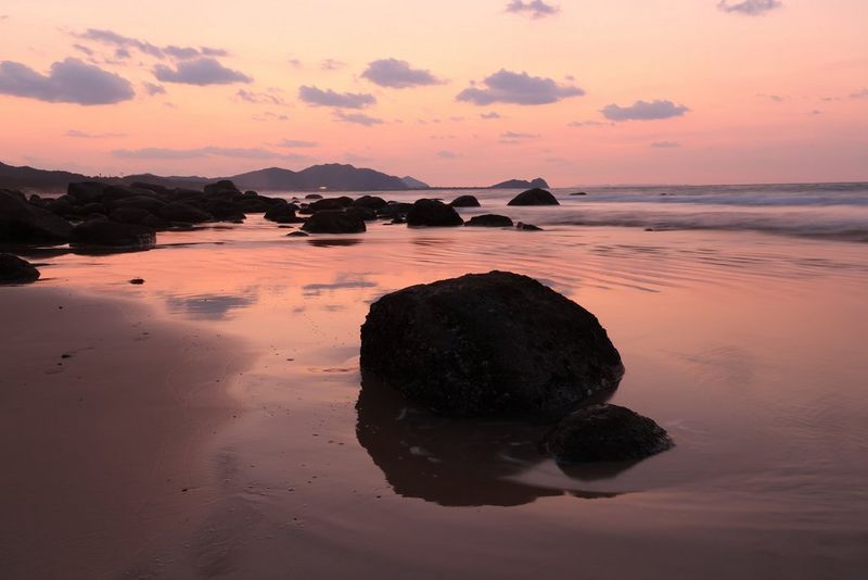 Large rocks on a beach, dark against the pinkish hue of the sand and sea, captured with a Canon RF-S 18-45mm F4.5-6.3 IS STM lens. 