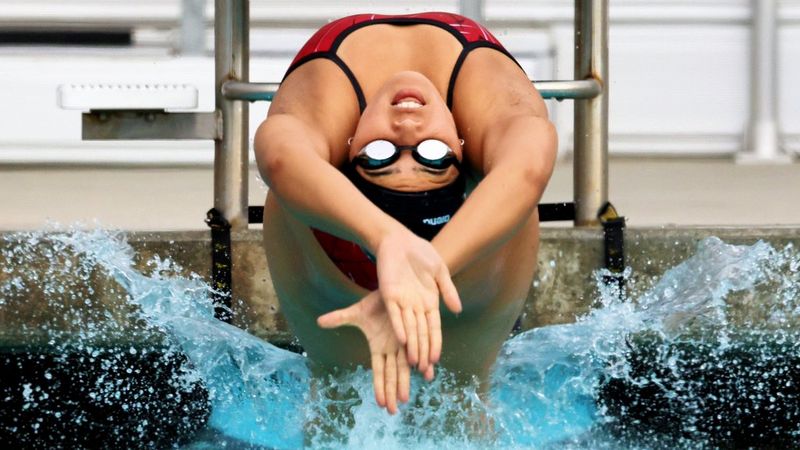 A swimmer leaps backwards into a pool with her arms outstretched creating an arc of water droplets.