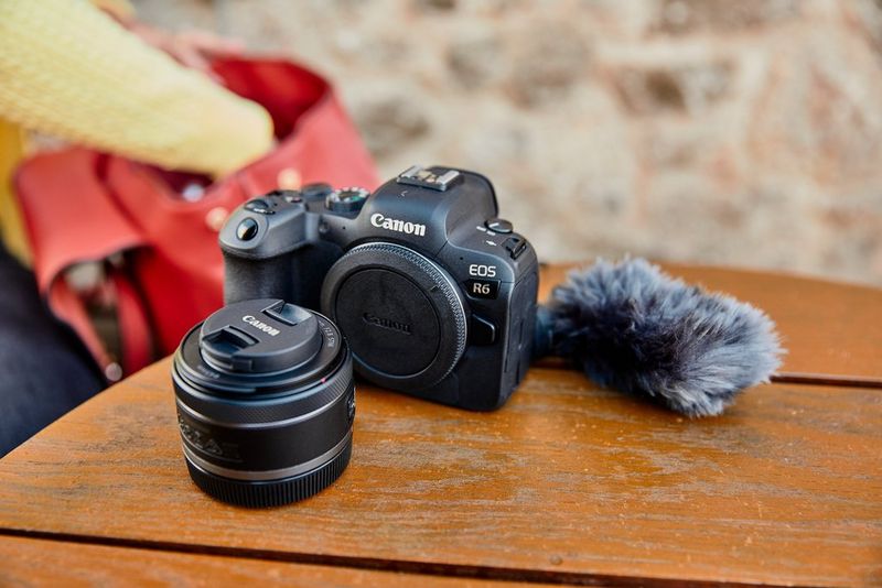 An EOS R6 camera, RF 16mm F2.8 STM lens and microphone sit on a wooden table outdoors.